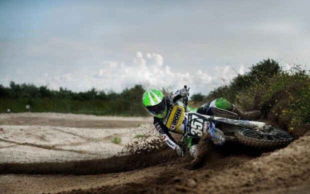 A rider in green gear navigates a sharp dirt curve on an enduro motorbike, kicking up dust, 2K Desktop Wallpaper