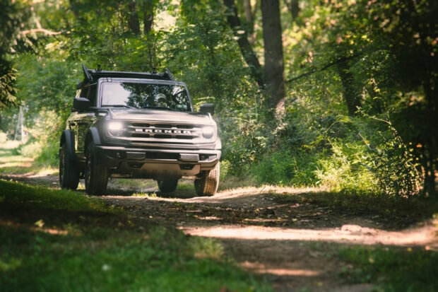 A rugged vehicle is driving through a dense forest trail showcasing off road driving, 2K Desktop Wallpaper