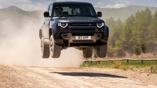 A black off road vehicle jumps over a dusty trail surrounded by trees with off road driving wallpapers, 2K Desktop Wallpaper
