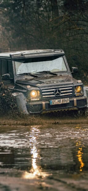 A rugged vehicle drives through muddy water in a forest during an off road driving adventure, HD Mobile Wallpaper