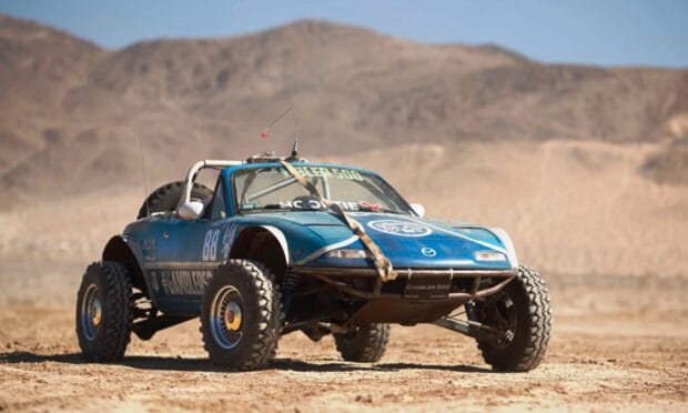 A blue rally raid vehicle is parked on a desert terrain with mountains in the background, HD Desktop Wallpaper