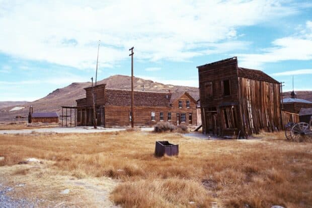 Old abandoned buildings stand in a dry field of a ghost town under a cloudy sky, HD Desktop Wallpaper