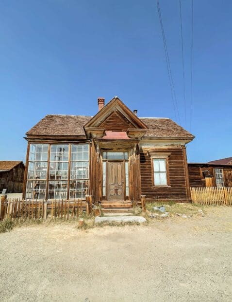 An old wooden house stands empty under a clear blue sky in a ghost town, 2K Mobile Wallpaper