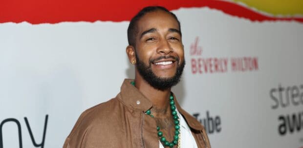 Omarion smiles warmly with a beaded necklace and brown jacket at a public event, 2K Desktop Wallpaper