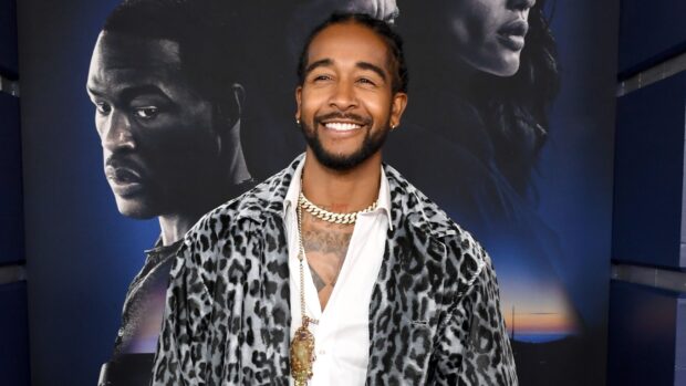 Omarion smiles wearing a leopard print jacket and gold chains in front of a poster, 2K Desktop Wallpaper
