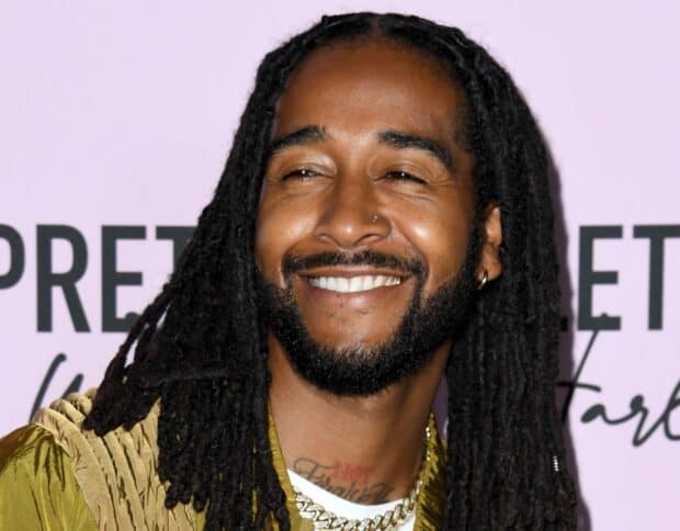 Omarion smiles warmly wearing gold chains and a stylish jacket, 2K Desktop Wallpaper