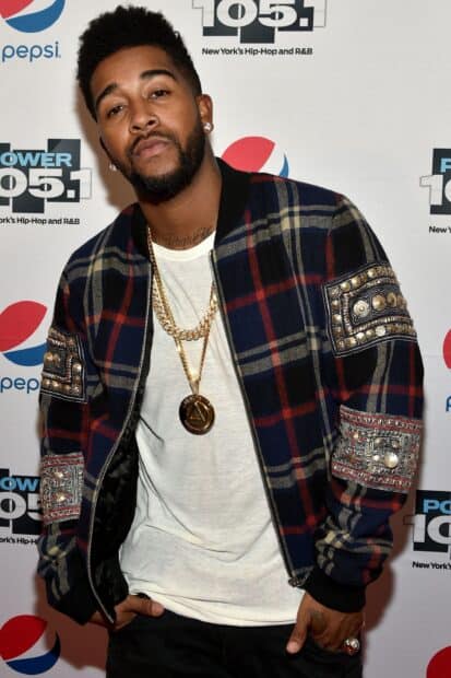 Omarion poses confidently wearing a plaid jacket and gold chains at an event, 2K Desktop Wallpaper
