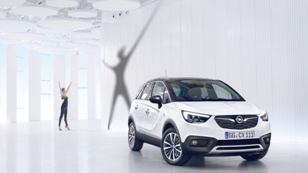 A white Opel Crossland is displayed in a bright modern showroom with a person and striking shadow, 4K Desktop Wallpaper