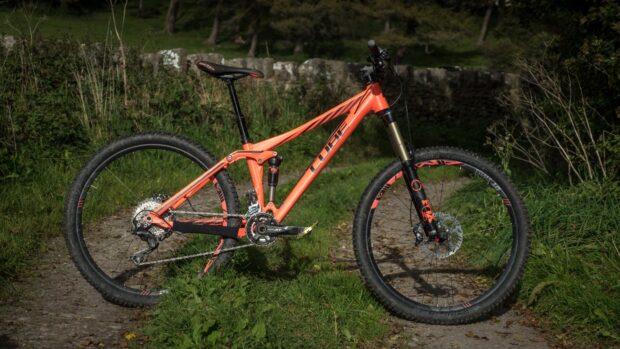 An orange Cube bike stands ready on a nature path surrounded by greenery, HD Desktop Wallpaper
