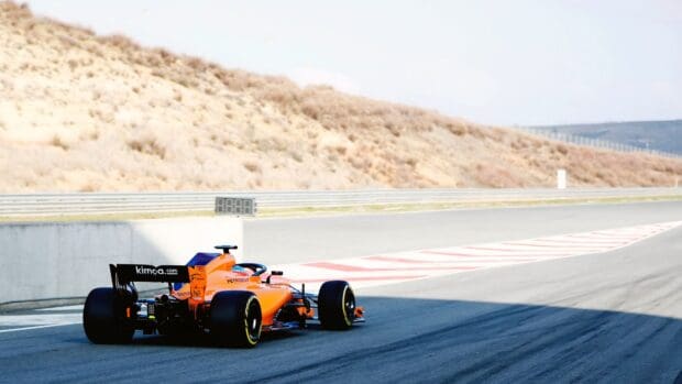 An orange Formula 1 car is driving on a racing track with dry hills in the background, 4K Desktop Wallpaper