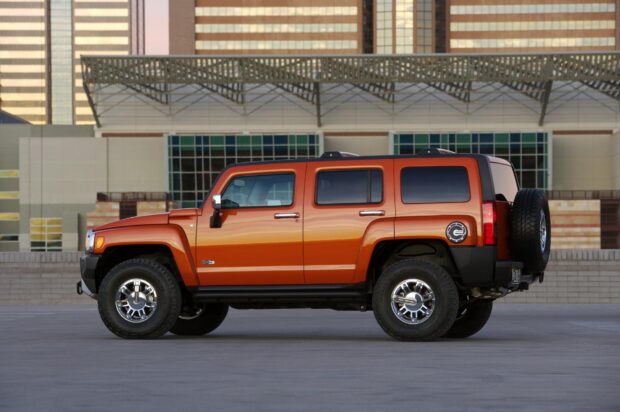A bright orange Hummer H3 is parked on an open concrete space with high rise buildings in the background, HD Desktop Wallpaper