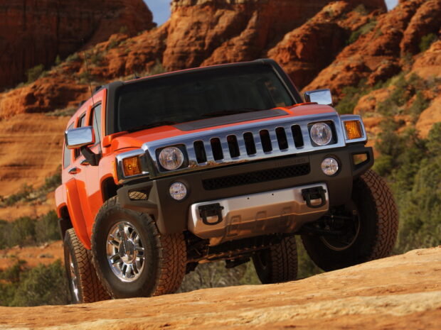 An orange Hummer H3 is navigating rocky terrain with a desert landscape in the background, HD Desktop Wallpaper