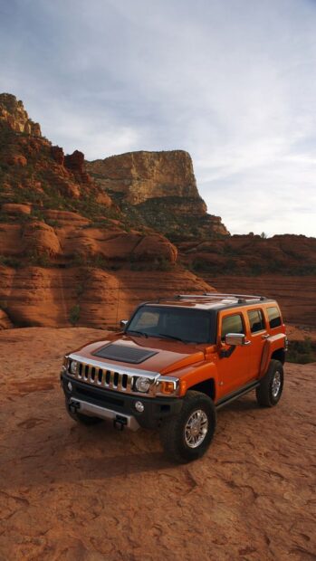 An orange Hummer H3 parked on rocky desert terrain with cliffs in the background, HD Phone Wallpaper