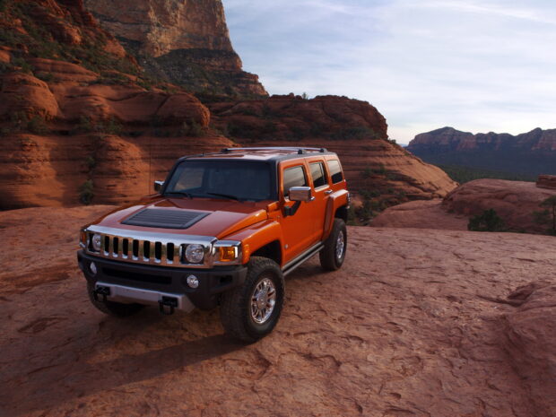 An orange Hummer H3 is parked on a rocky desert landscape with red cliffs in the background, HD Desktop Wallpaper