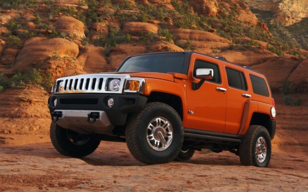 An orange Hummer H3 is parked on rugged desert terrain with rock formations in the background, HD Desktop Wallpaper