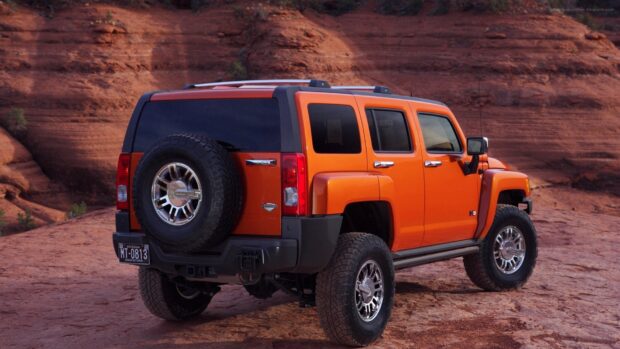 An orange Hummer H3 is parked on rocky desert terrain with red cliffs in the background, HD Desktop Wallpaper