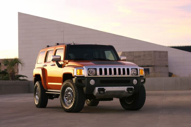 An orange Hummer H3 is parked on a concrete surface near modern architecture at sunset, 2K Desktop Wallpaper