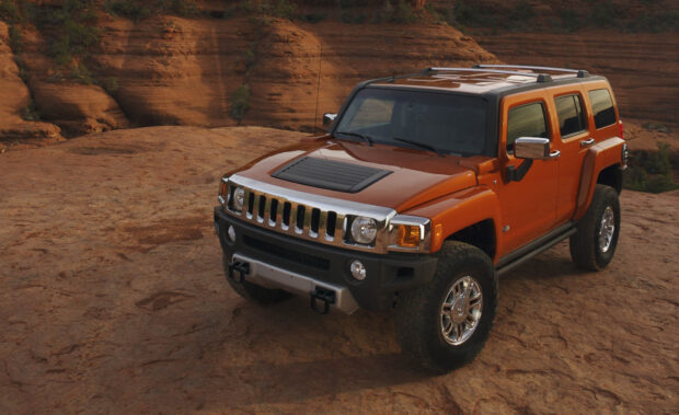 An orange Hummer H3 is parked on rocky terrain with natural red cliffs in the background, HD Desktop Wallpaper