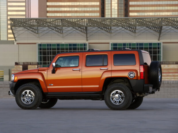 A bright orange Hummer H3 is parked on a concrete surface in front of a modern building, HD Desktop Wallpaper