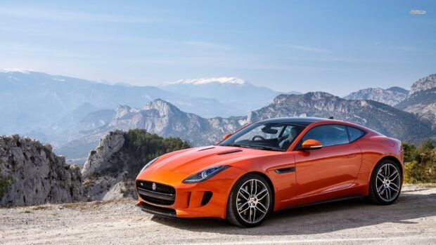 An orange Jaguar F Type is parked on a gravel road with mountains and clear sky in the background, HD Desktop Wallpaper