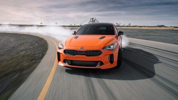 A bright orange Kia Stinger is drifting skillfully on a racetrack with smoke trailing behind, 2K Desktop Wallpaper