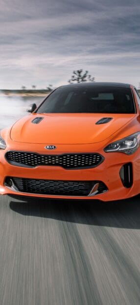 A sleek orange Kia car is driving on the road under a cloudy sky, HD Mobile Wallpaper