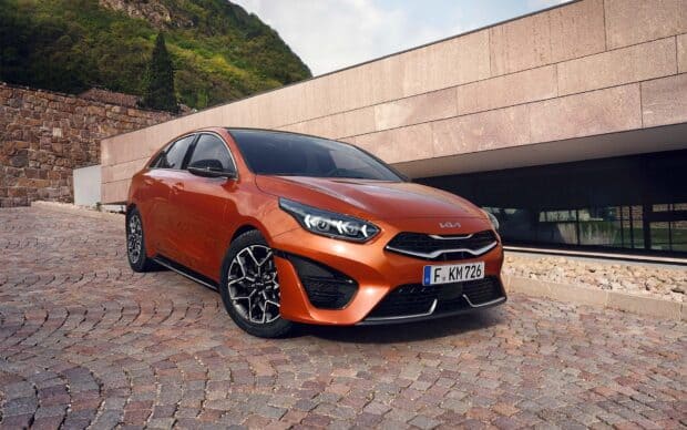 An orange Kia car is parked on a cobblestone driveway near a modern building with greenery, HD Desktop Wallpaper