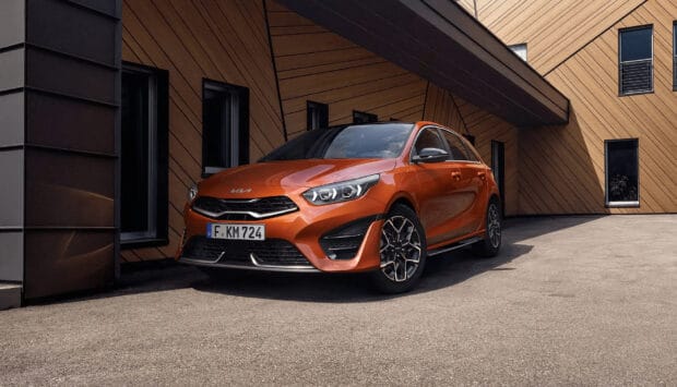 Orange Kia model is parked in front of a wooden geometric patterned building under clear skies, HD Desktop Wallpaper
