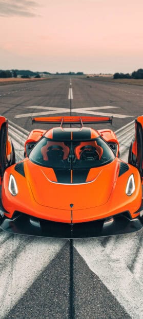 A bright orange Koenigsegg is parked on an empty runway with its doors open, 2K Phone Wallpaper