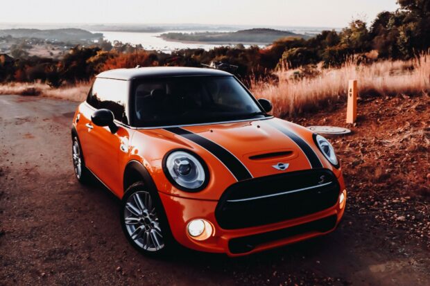 The orange Mini Cooper is parked on a rural road with a scenic background, 2K Desktop Wallpaper