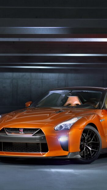 The orange Nissan GT R is parked inside a dimly lit garage with reflective surfaces, 4K Phone Wallpaper