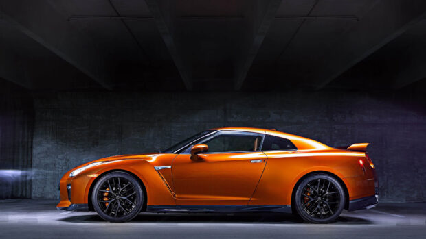 A bright orange Nissan GT R sports car is parked inside a dimly lit concrete garage, 4K Desktop Wallpaper