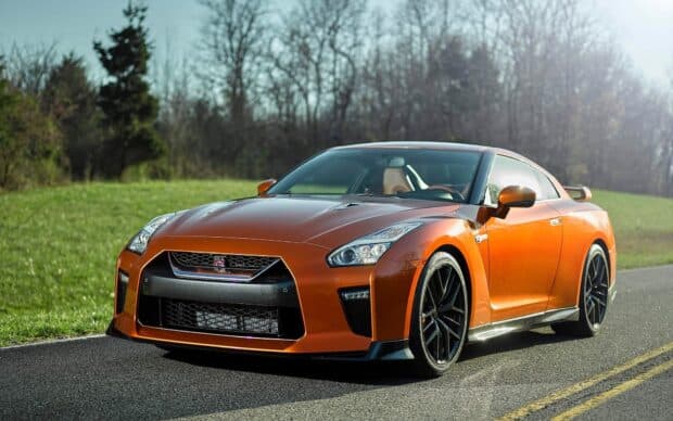 An orange Nissan GT R sports car is parked on a sunny roadside with trees in the background, HD Desktop Wallpaper