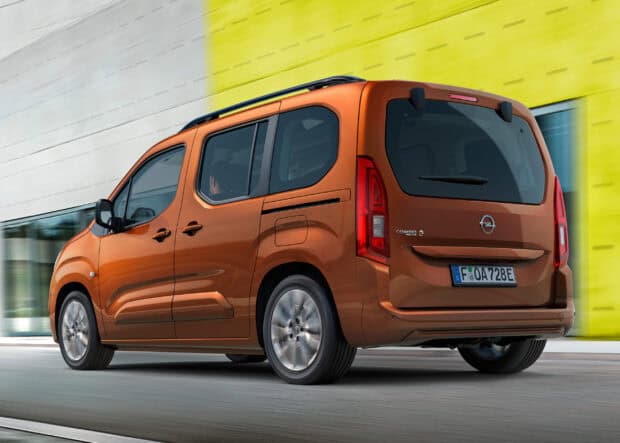 An orange Opel Combo is seen from behind driving near a yellow and white building, 2K Desktop Wallpaper
