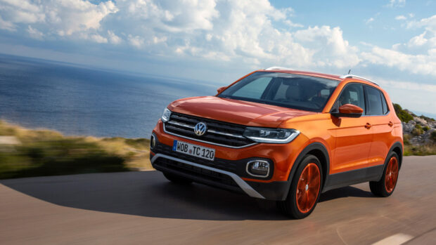 An orange Volkswagen T Cross is driving along a coastal road under a cloudy sky, 4K Desktop Wallpaper