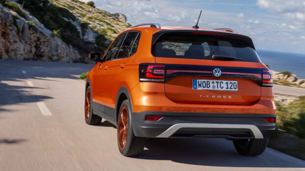 A bright orange Volkswagen T Cross is shown driving on a winding coastal road near the ocean, HD Desktop Wallpaper