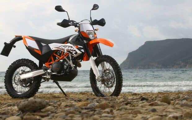An enduro motorbike is parked on a rocky beach with the sea and cliffs in the background, HD Desktop Wallpaper