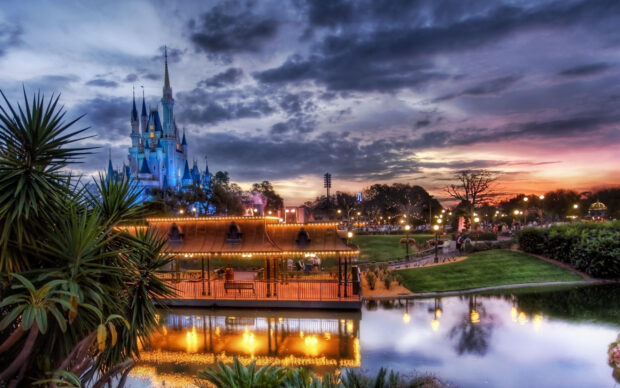 The Orlando castle is beautifully lit at sunset with a calm reflective pond nearby, 2K Desktop Wallpaper