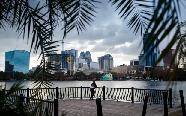 A person leans on a railing overlooking the Orlando skyline across the lake under cloudy skies, HD Desktop Wallpaper