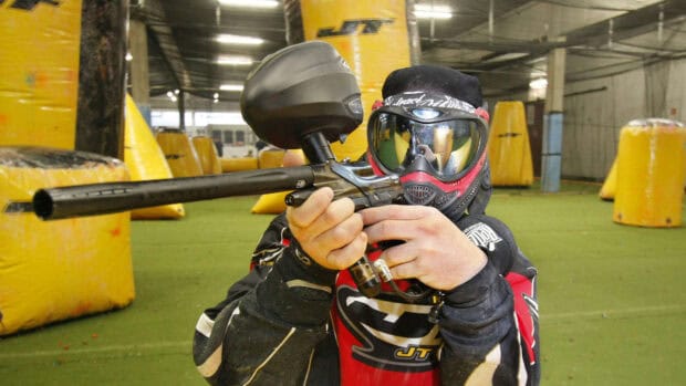 A paintball player wearing protective gear aims a marker in an indoor arena, HD Desktop Wallpaper