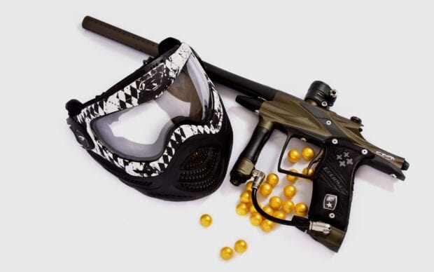 A paintball gun and protective mask are placed next to yellow paintballs on a white surface, 2K Desktop Wallpaper
