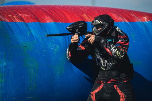 A paintball player wearing protective gear is aiming during a match on a paintball field, HD Desktop Wallpaper