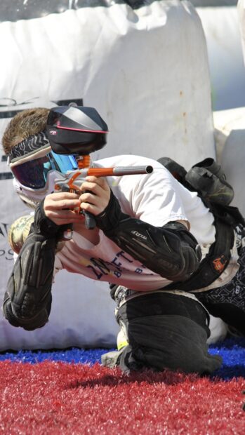 A paintball player is crouched and aiming a paintball marker during a match, HD Mobile Wallpaper