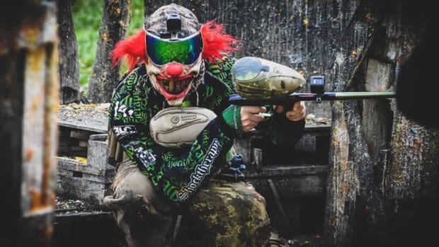A paintball player in a creepy clown mask aiming with a paintball gun during a match, HD Desktop Wallpaper