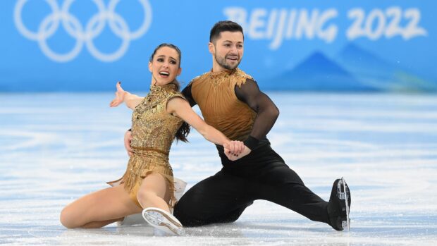 A pair performing elegant ice dancing at the Olympics during a competition with Olympic rings in the background, 2K Desktop Wallpaper