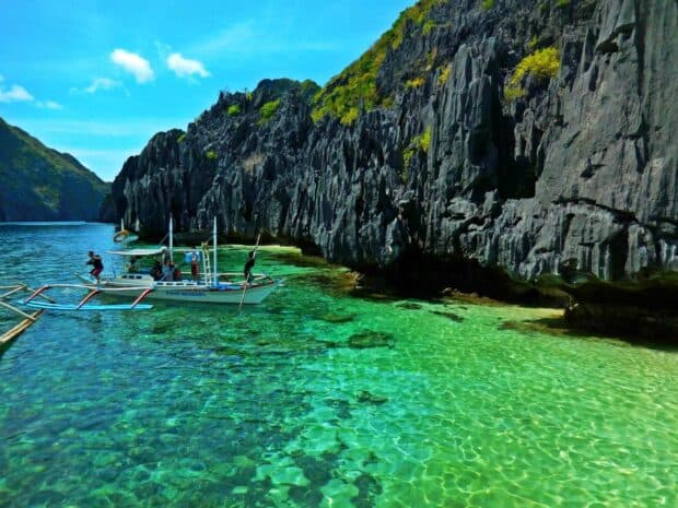 A boat with tourists explores the clear green water by rocky cliffs in Palawan, Philippines, HD Desktop Wallpaper