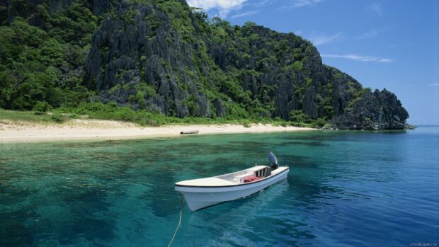 A boat floats on clear water near the rocky shore of Palawan with green trees, HD Desktop Wallpaper