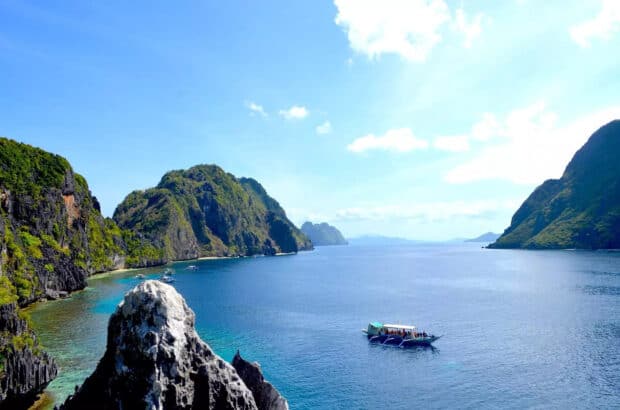 A boat floats on clear blue water near lush green cliffs in Palawan, HD Desktop Wallpaper