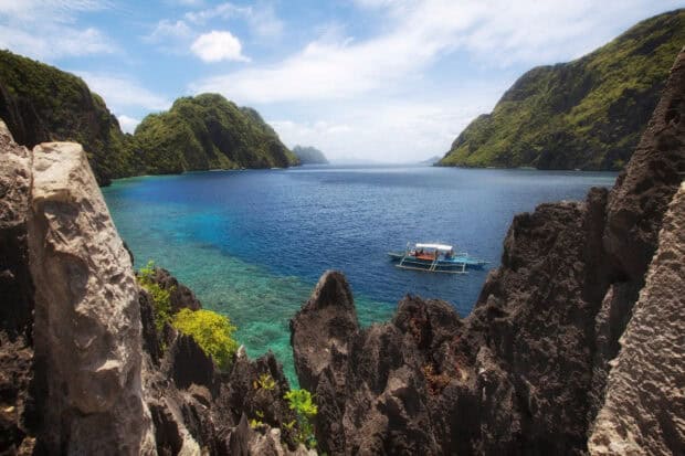 A boat floats on clear blue waters surrounded by rocky cliffs in Palawan landscapes, 2K Desktop Wallpaper