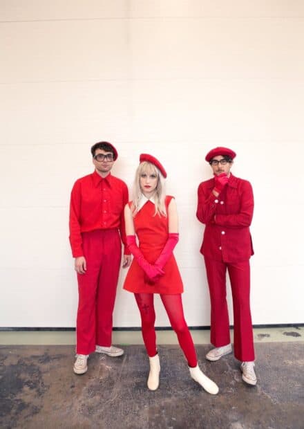 The Paramore members are wearing coordinated red clothing and posing against a white wall, HD Portrait Wallpaper